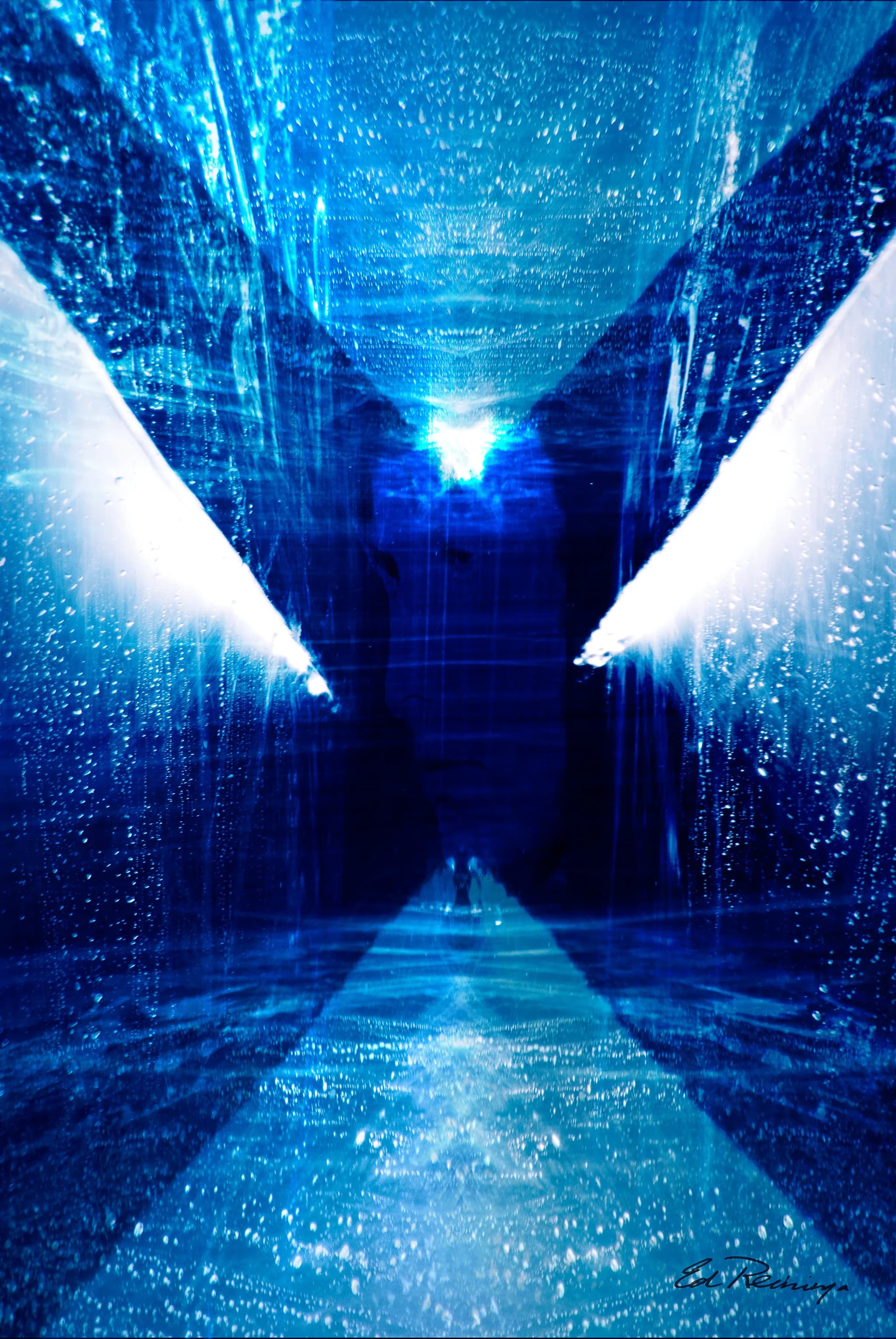 Abstract photograph in deep blue: a corridor of glassy, streaked walls converging on a bright white light, with a small dark figure on the floor below it.